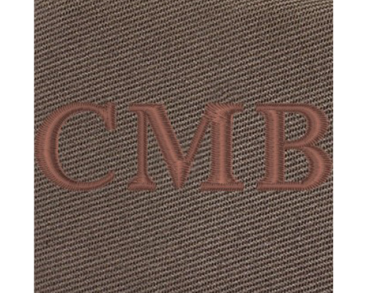 The Travis Tote Bag Cotton Twill: Close-up of brown textured fabric with CMB embroidered, showcasing personalized whiskey embroidery on durable, versatile tote.