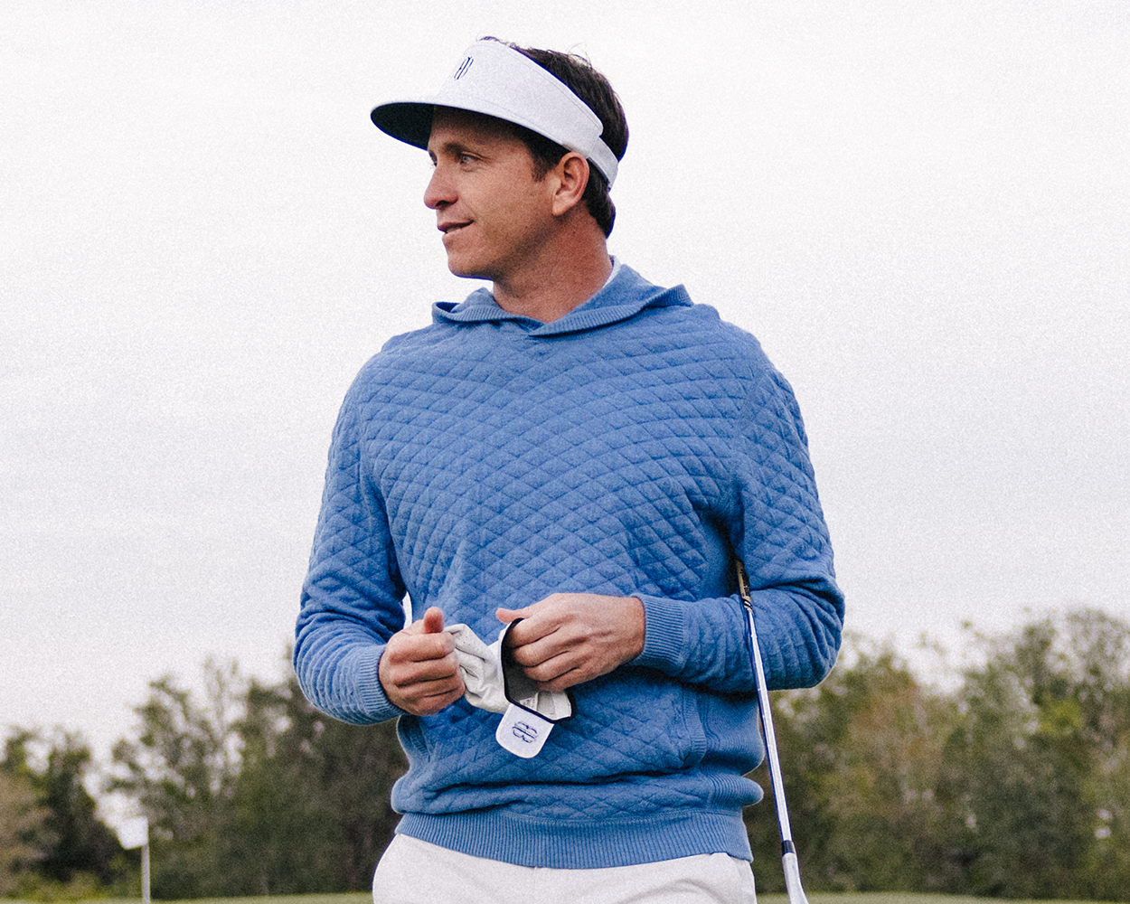 Man on golf course wearing The Cocktail Tour Visor: White with HB Icon, holding a golf club and towel, showcasing its high crown design.