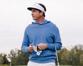 Man on golf course wearing The Cocktail Tour Visor: White with HB Icon, holding a golf club and towel, showcasing its high crown design.