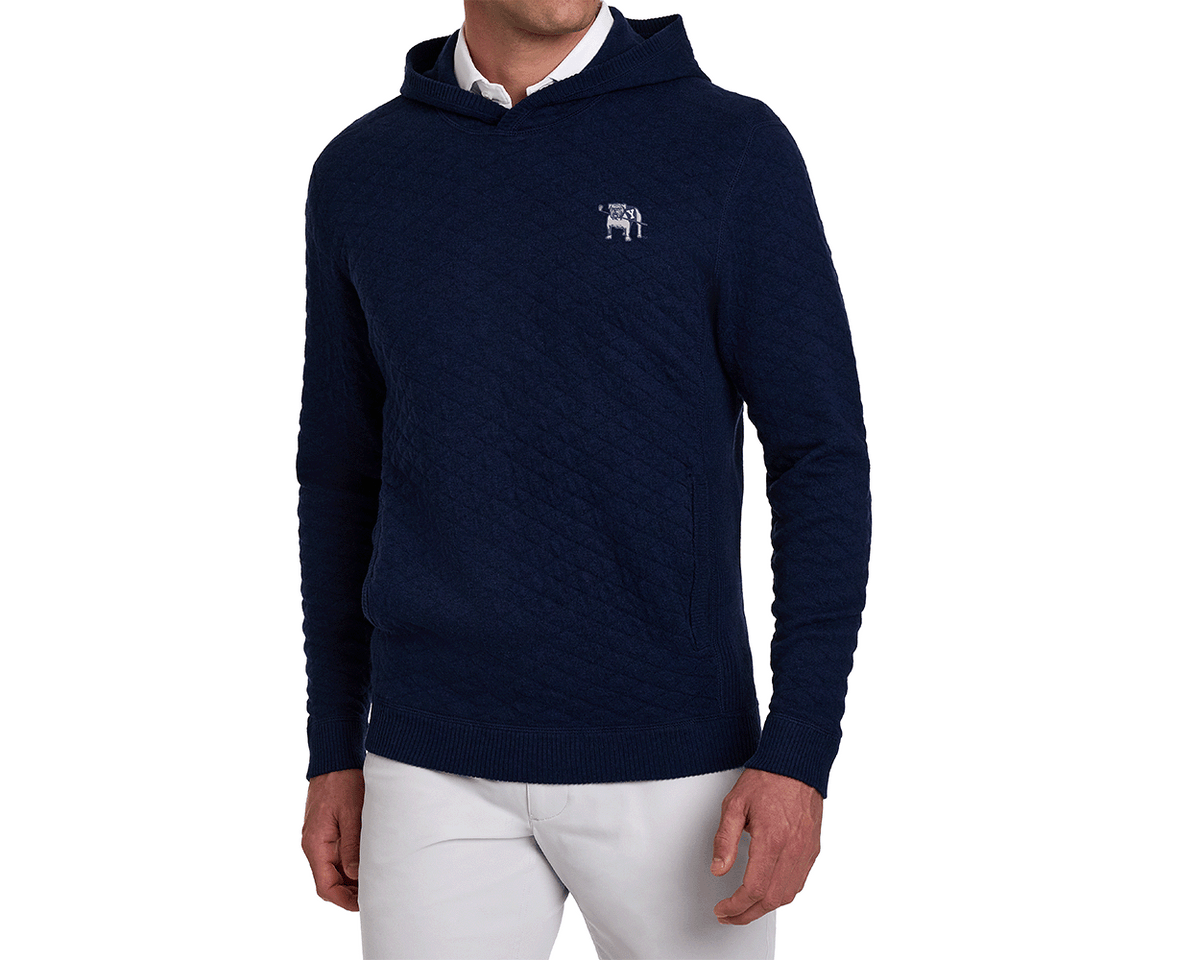 Model wearing the Yale Golf Course Wallace Sweater: Heathered Navy, a quilted pullover with a kangaroo pocket and embroidered bulldog logo, paired with light trousers.