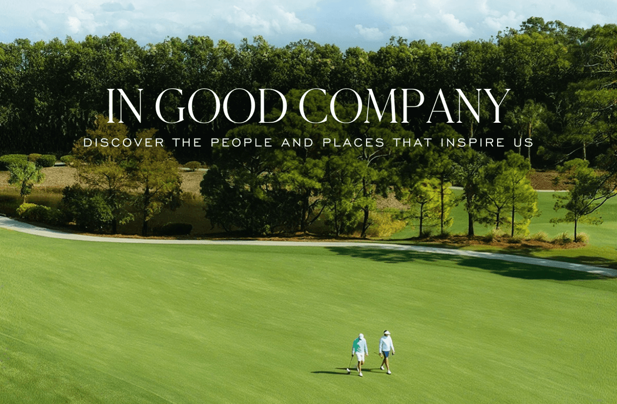 Two golfers in teal and white walking a green fairway lined with pines, under the title "IN GOOD COMPANY" and "DISCOVER THE PEOPLE AND PLACES THAT INSPIRE US".