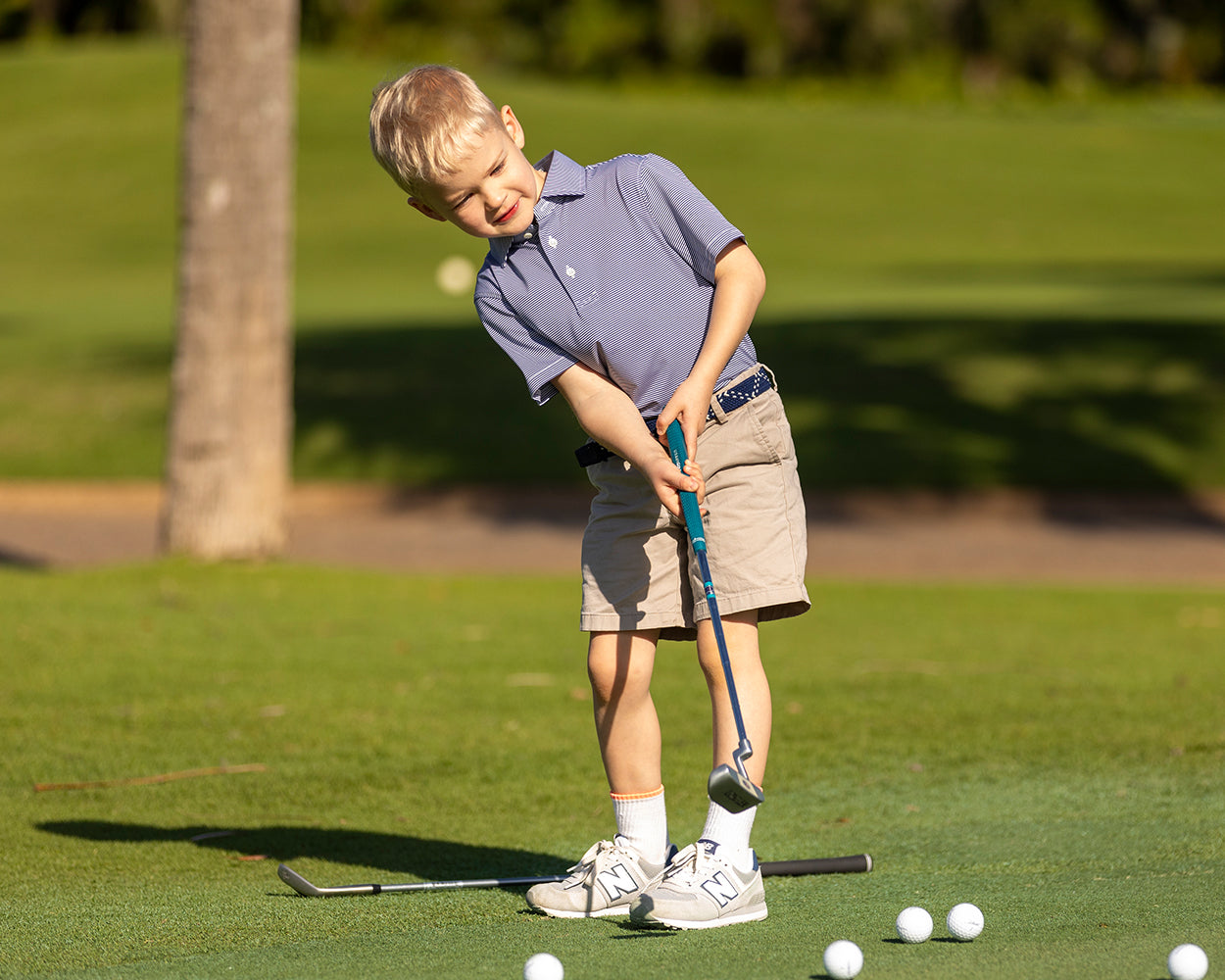 Young boy on putting green in The Perkins Boys Shirt, showcasing its structured spread collar and performance fabric, lining up a golf stroke with putter.