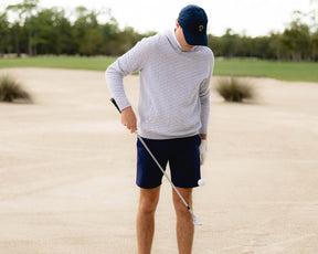Golfer in sand bunker wearing The Wallace Hoodie Sweater: Heathered Gray, showcasing its quilted design and ribbed side panels, holding an iron club.